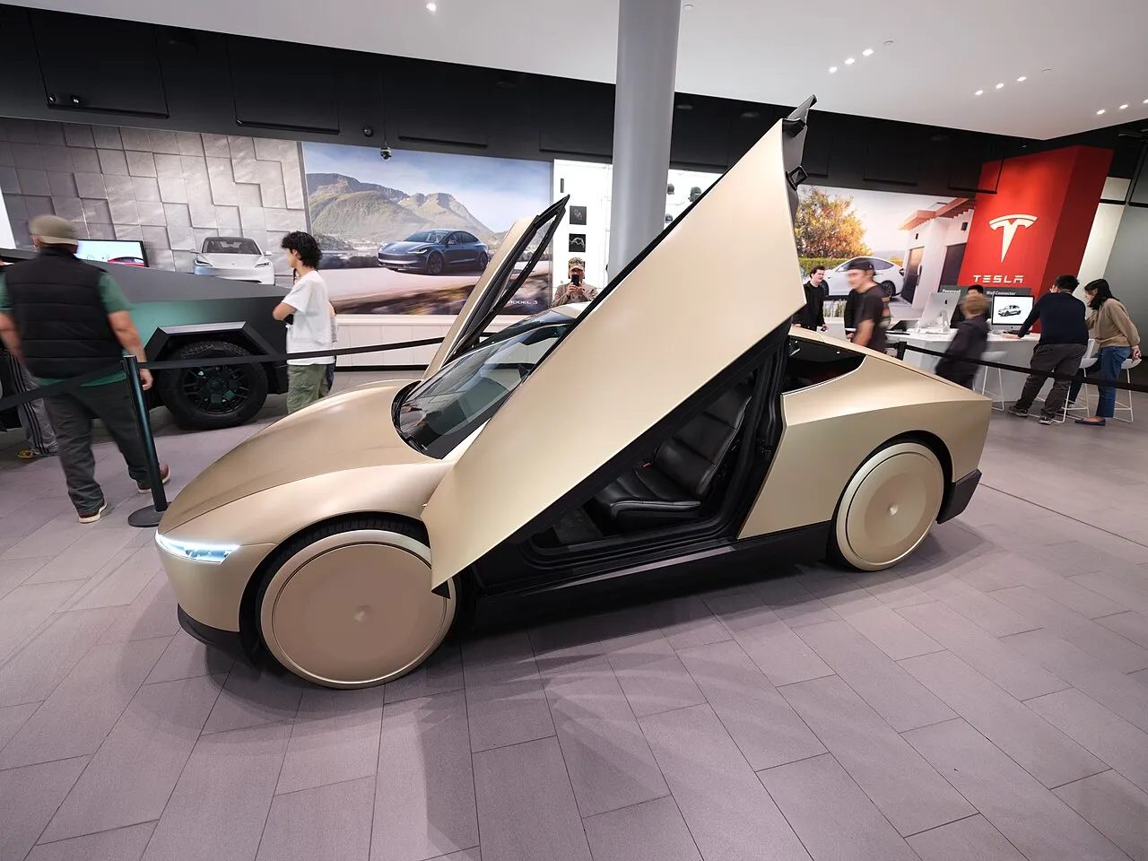 Champagne-gold Tesla Cybercab on display in a Tesla showroom, side view with its butterfly door raised