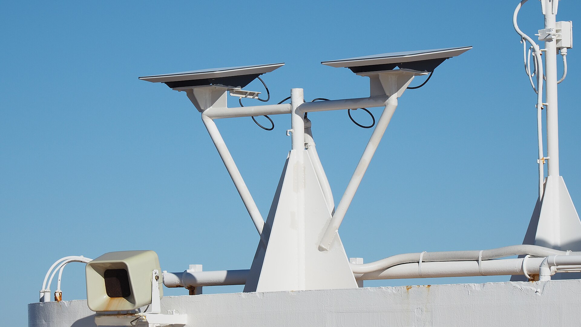 Two flat, rectangular Starlink dishes mounted on a white steel frame on top of a ship, against a clear blue sky