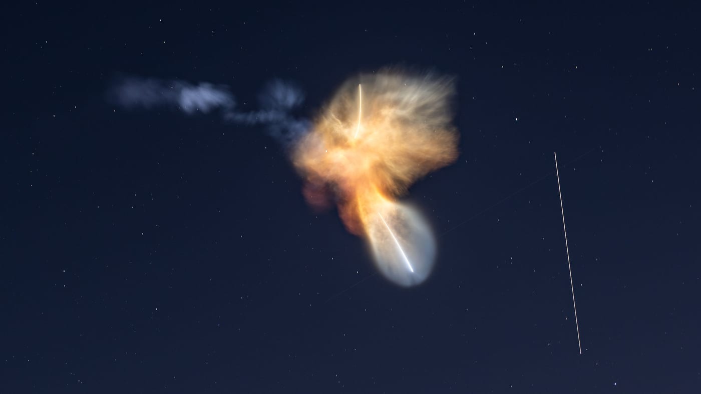 A long-exposure night photo of a Falcon 9 launch, with the first stage turning back toward the Cape and the International Space Station crossing the sky as a thin streak