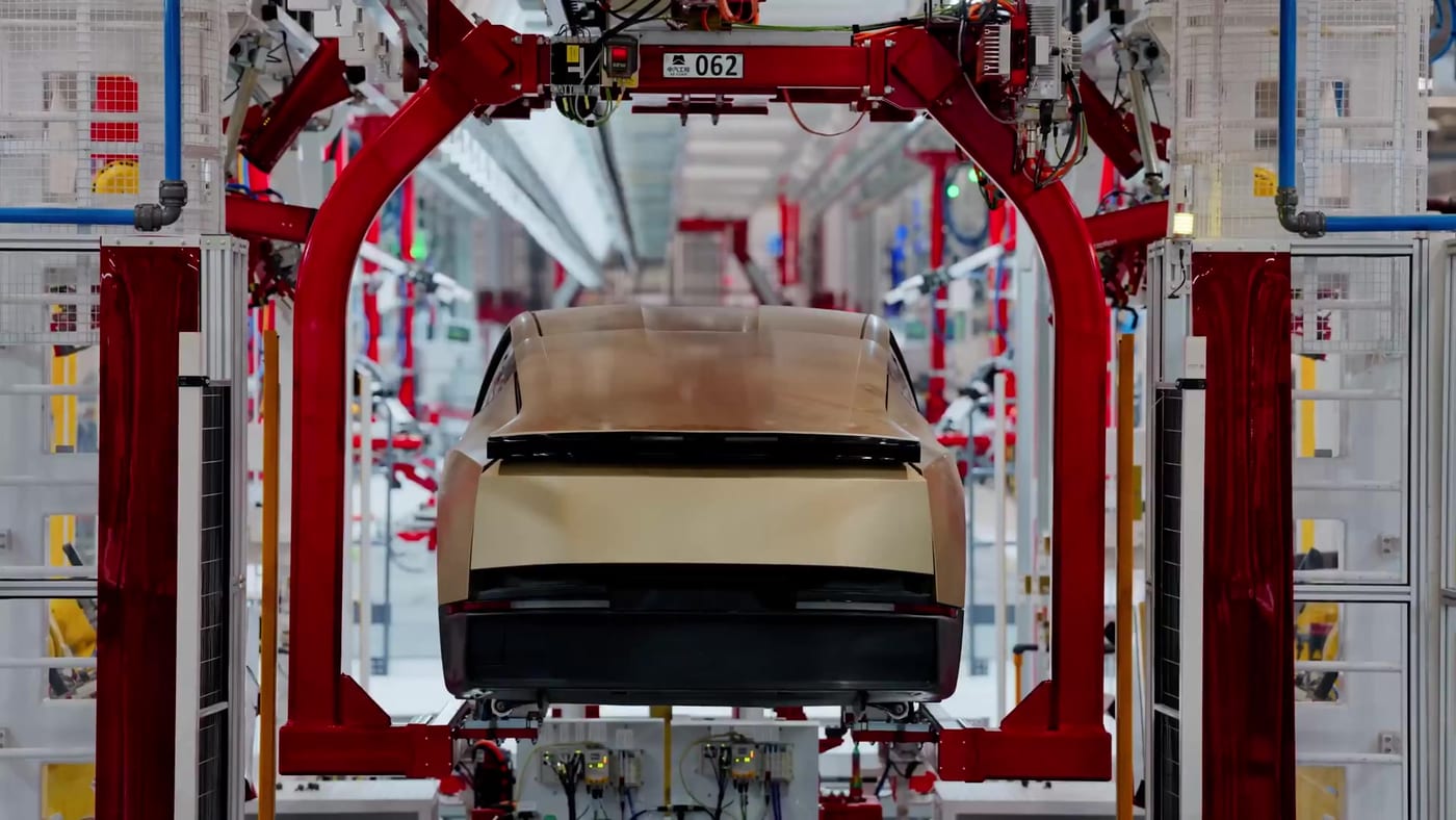 A gold Tesla Cybercab, seen from behind, moving through a red gantry on the factory line