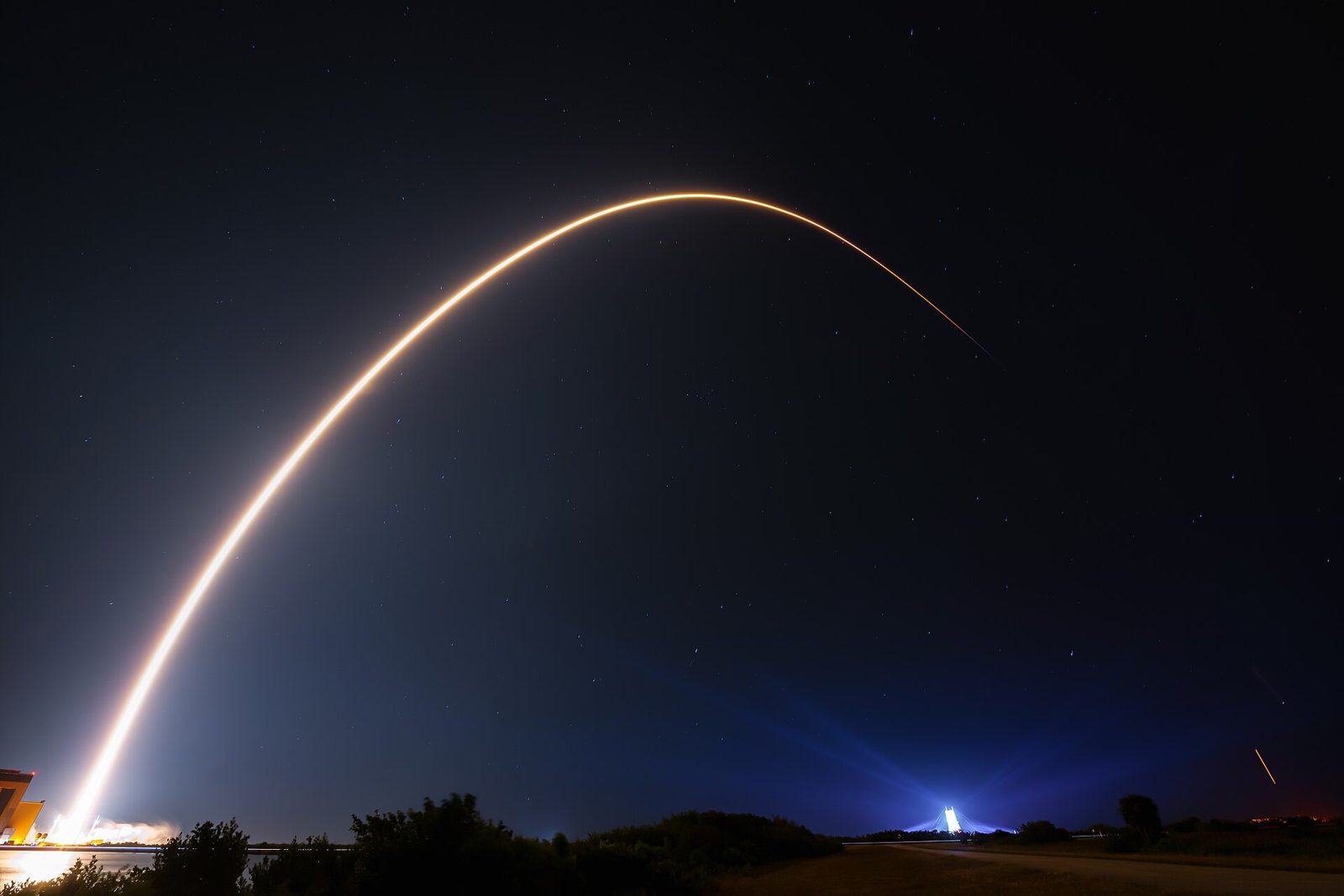 Long-exposure photo of a Falcon 9 launch from Space Launch Complex 40 at night, its bright arc curving across a starry sky over Cape Canaveral