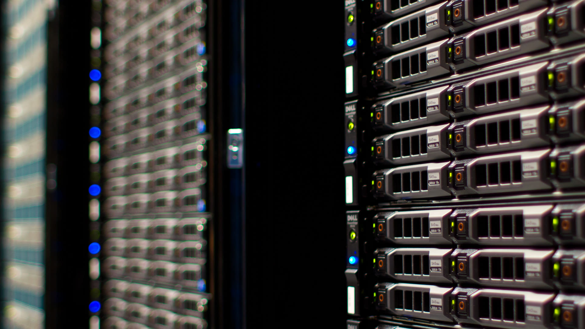Close-up of a dark data center aisle with rows of rack-mounted servers, their front panels lit by small blue and green status lights