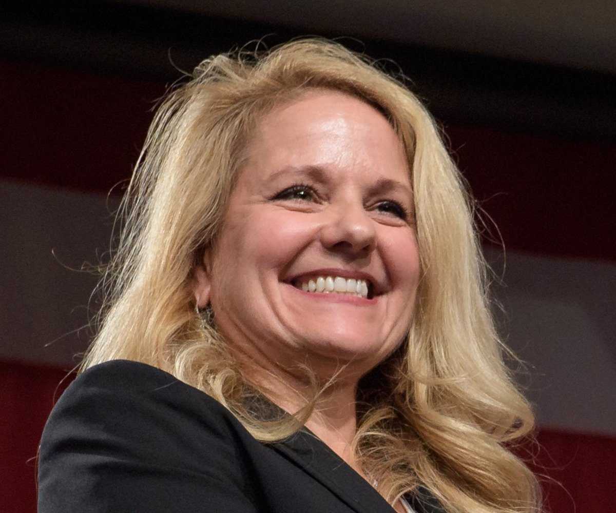 SpaceX President and COO Gwynne Shotwell smiling on stage in front of an American flag