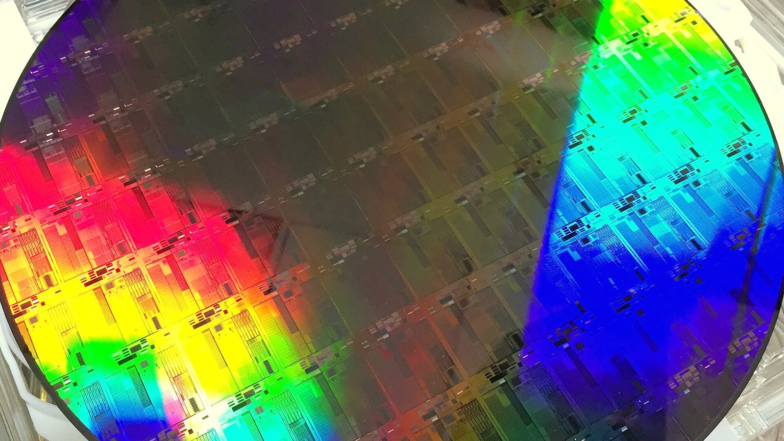 Close-up of a 300mm silicon wafer covered in a grid of rainbow-reflecting chip dies