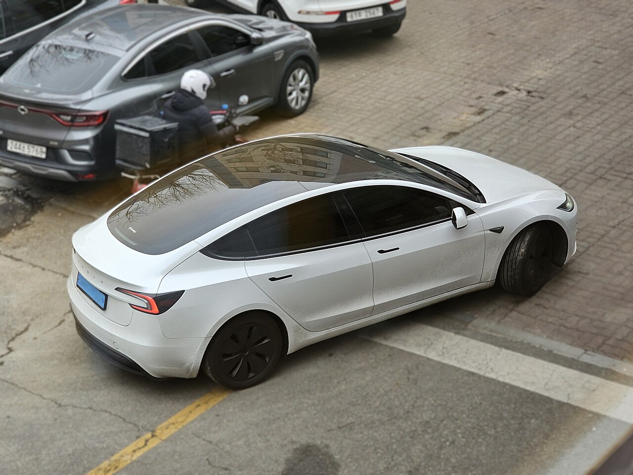 A Pearl White Tesla Model 3 Highland parked outside