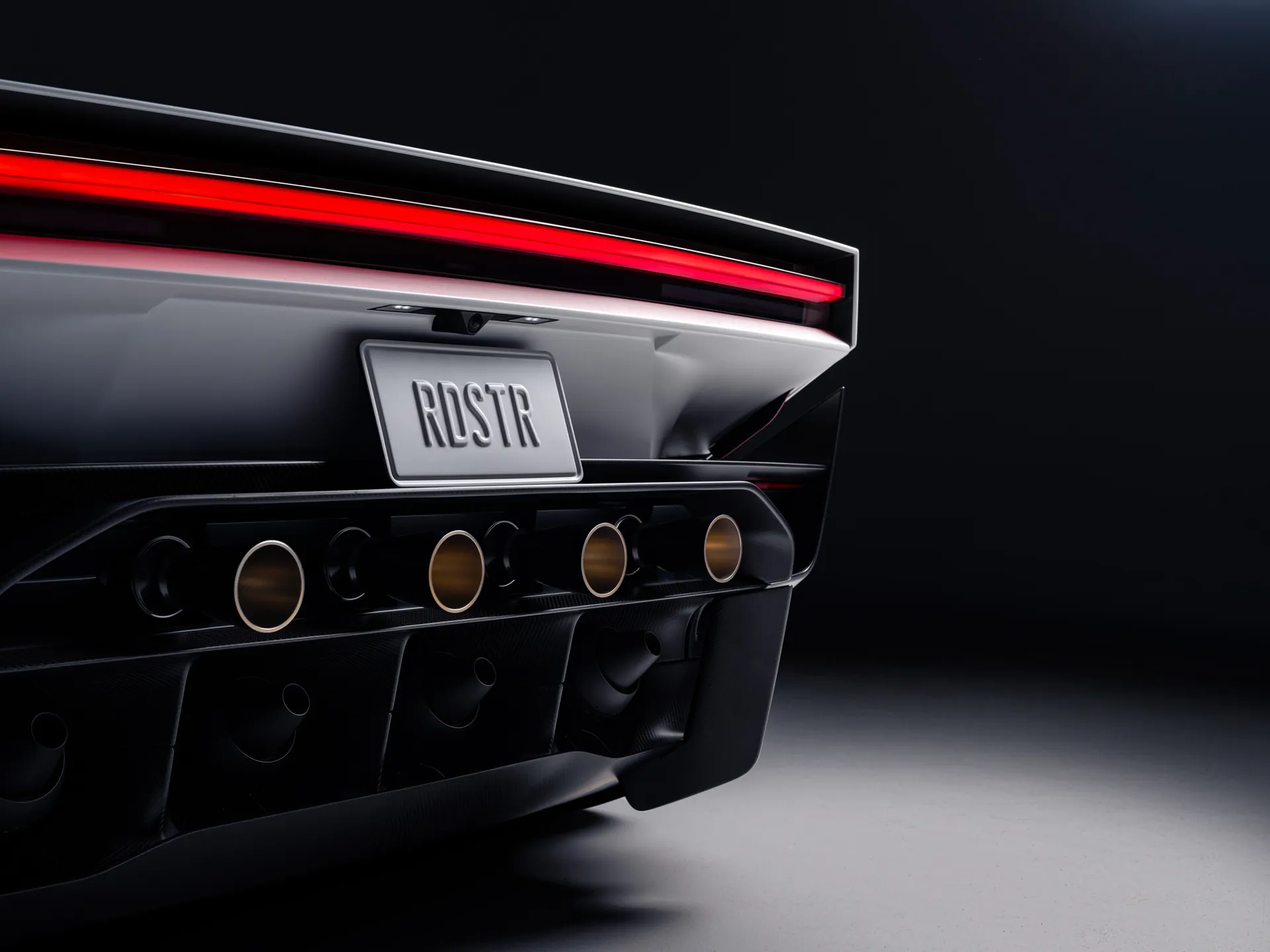 Rear of the Tesla Roadster in the dark: full-width red light bar, RDSTR plate and a row of cold-gas thruster nozzles