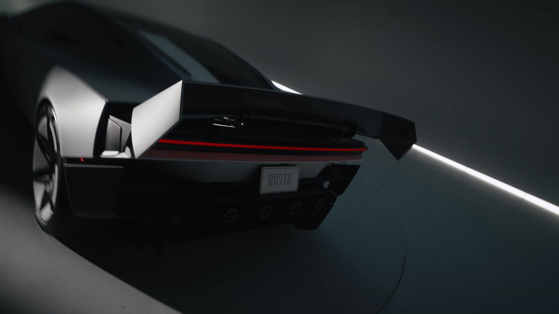 Rear three-quarter view of the Roadster in a dark studio, rear wing and red light bar visible